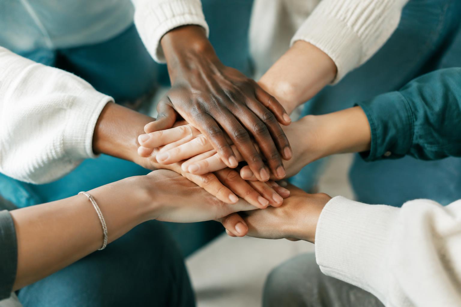 A circle of hands stacked together in the middle — people standing with each other.